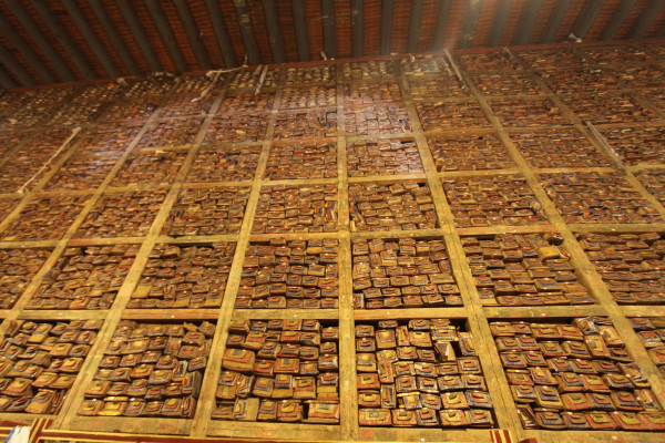 Looking up at a very tall wall of books/scrolls inside of small boxes which are grouped inside of cubes. Everything is mostly brown with splashes of bright colors.