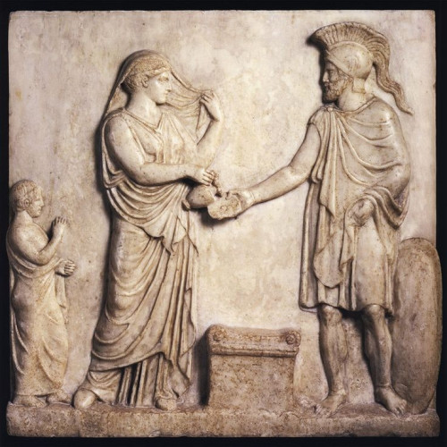 Aphrodite, dressed in a long chiton or peplos with a veil is holding it in the manner of brides while pouring a libation over an altar into the phiale held by her lover Ares, dressed in a chiton and himation but with armour in the form of a crested helmet and his leg guards. A shield leans on the ground to his right. A child or servant stands behind Aphrodite to the left.