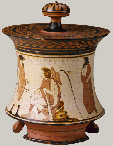 White-ground terracotta pyxis with a red figure vase painting of the Judgement of Paris. Paris is seated on a rock wearing a traveller's hat, a short chlamys cloak, and boots. He holds a club in his left. Hermes approaches from the left, a bearded god with his iconic kerykeion staff and winged sandals.