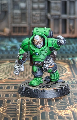 Warhammer 40k Leagues if Votann Kill Team miniature painted with green armor and orange guns and lots of metallic silver bits around. He's lobbing grenades like a maniac.