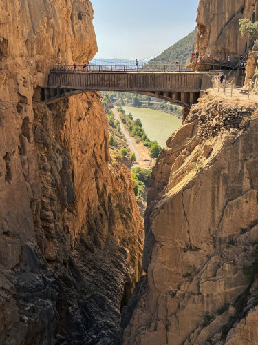 Foto vertical en la que se ve el puente colgante del Caminito del Rey, que une ambas paredes en un cañón de rocas con precipicio enorme y el río abajo del todo.