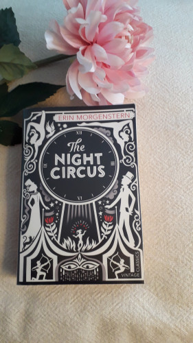 The cover of The Night Circus, illustrated in black and white, shows the silhouettes of a man and a woman, a large clock and some circus performers.