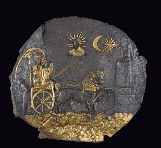 One of the oldest antiquities found at Aï Khanum, this spectacular disk depicts Cybele, the goddess of nature, and Nike, the personification of Victory, on a chariot drawn by two lions through a mountainous landscape. It is a remarkable example of hybrid Greek and Oriental imagery that typified the arts of Hellenized Asia. Ancient Near Eastern features include: the parasol—a royal symbol—here held by a priest; the stepped altar; the shape of the chariot; the scalloped pattern indicating mountainous terrain; and the moon crescent and the star. The cult of Cybele originated in Anatolia but had long been adopted by the Greeks. Also borrowed from the Greek tradition are the representation of the winged Nike, the bust of the sun god Helios, and the naturalistic rendering of the drapery and the lions. The overall composition of the scene, however, lacking any indication of perspective, is more typical of Near Eastern art.