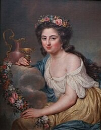 A painted portrait of Henriette Julie Herz (nee de Lemos). She is sieated, looking directly and the viewer, her long wavy hair flowing down her back, a flower crown on her head. She wears a loose gauzy gown, with one shoulder exposed. 