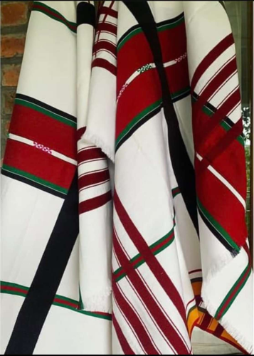 A handcrafted, woven cloth hung on the wall. It has red, green, and black stripes with white in color.