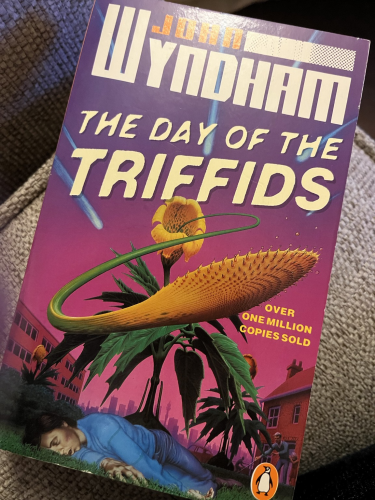 Front cover of The Day of the Triffids Penguin edition featuring a plant with sucker flying out and a dead body laying at it’s base.