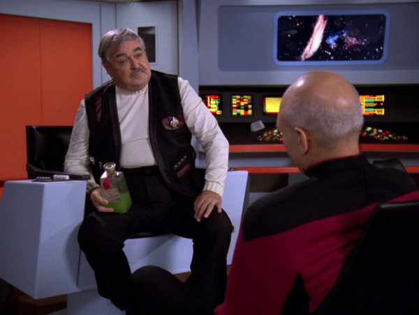 Scotty sitting in the captain’s chair with a bottle of alcohol and talking to Picard 