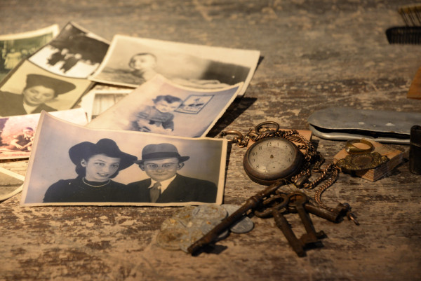 Some photographs, a broken pocket watch, coins and set of keys on a table. The objects belonged to victims of Auschwitz.