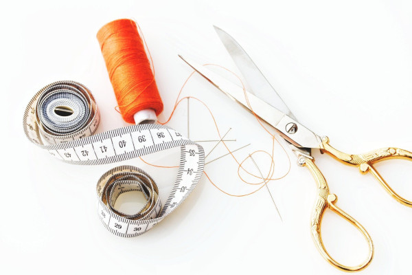 Silver scissors with gold handles, a spool of oranges thread, and a tailor's measuring tape.