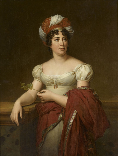 A painted portrait of Germaine de Stael. she looks up and to the right, away from the viewer. She wears an off the shoulder white dress with a princess waist, an enamel cameo portrait at her bust. She has a red and white turban on her head, hiding her curly brown hair.