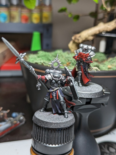 Two Warhammer 40k Adepta Sororitas minis partially painted. Purple robes with red lining, silver armor, red casing on the guns.