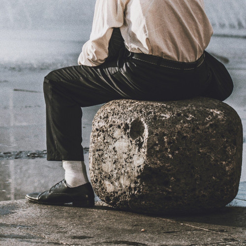 A person sitting on a boulder beside water