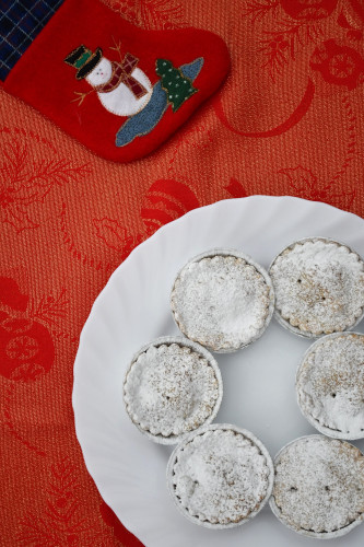 A plate of mince pies on a festive tablecloth next to a christmas stocking.