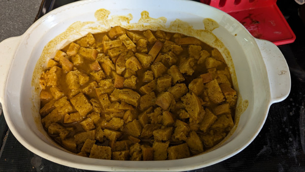 A white oblong baking dish filled with cubes of bread soaking in the pumpkin custard mixture