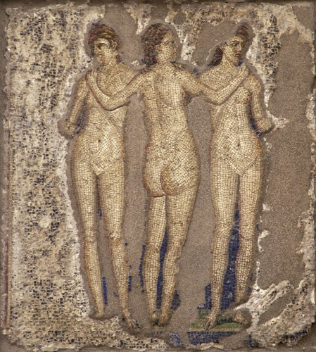 Three women standing in the nude. The central figure faces away from the viewer and reaches out to touch the outer shoulders of the other two women. Each looks off into her own middle distance. The background of the mosaic is quite damaged but some dark blues and greens can be seen.