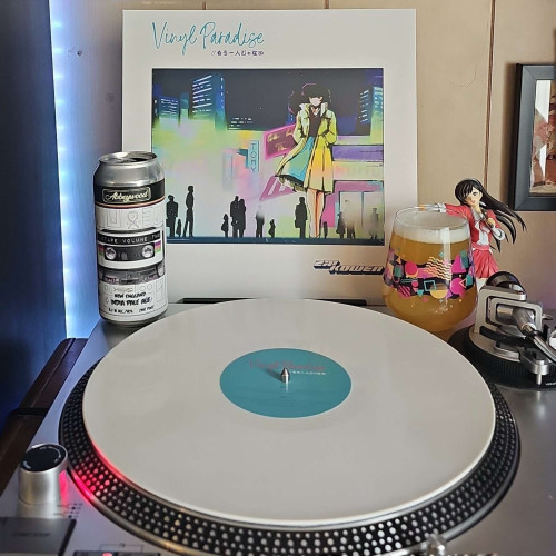A Virgin White vinyl record sits on a turntable. Behind the turntable, a vinyl album outer sleeve is displayed. The front cover shows an anime girl walking through an urban area at night, while wearing a long coat. 

In front of the album cover is a 16oz beer can featuring a cassette tape, and a stemless glass filled with beer. To the right of the album cover is an anime figure of Yuki Morikawa singing in to a microphone and holding her arm out.