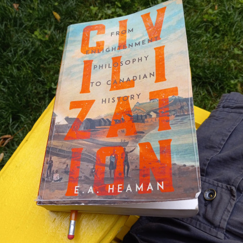 A paperback copy of E.A. Heaman's Civilization: From Enlightenment Philosophy to Canadian History with a peeling and dog-eared cover. It is sitting on the arm of a yellow wooden chair with green grass below.